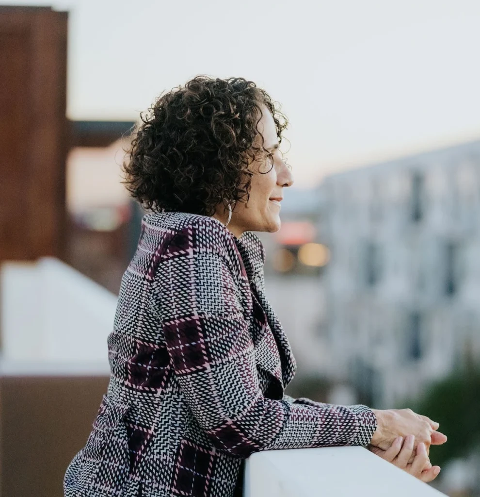 Dominique DelHomme leaning on a rooftop ledge, the city behind her